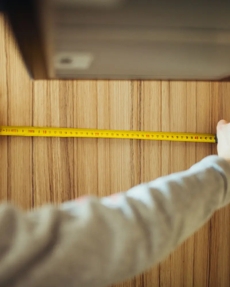 Zwei Hände messen mit einem Maßband eine Holzwand aus