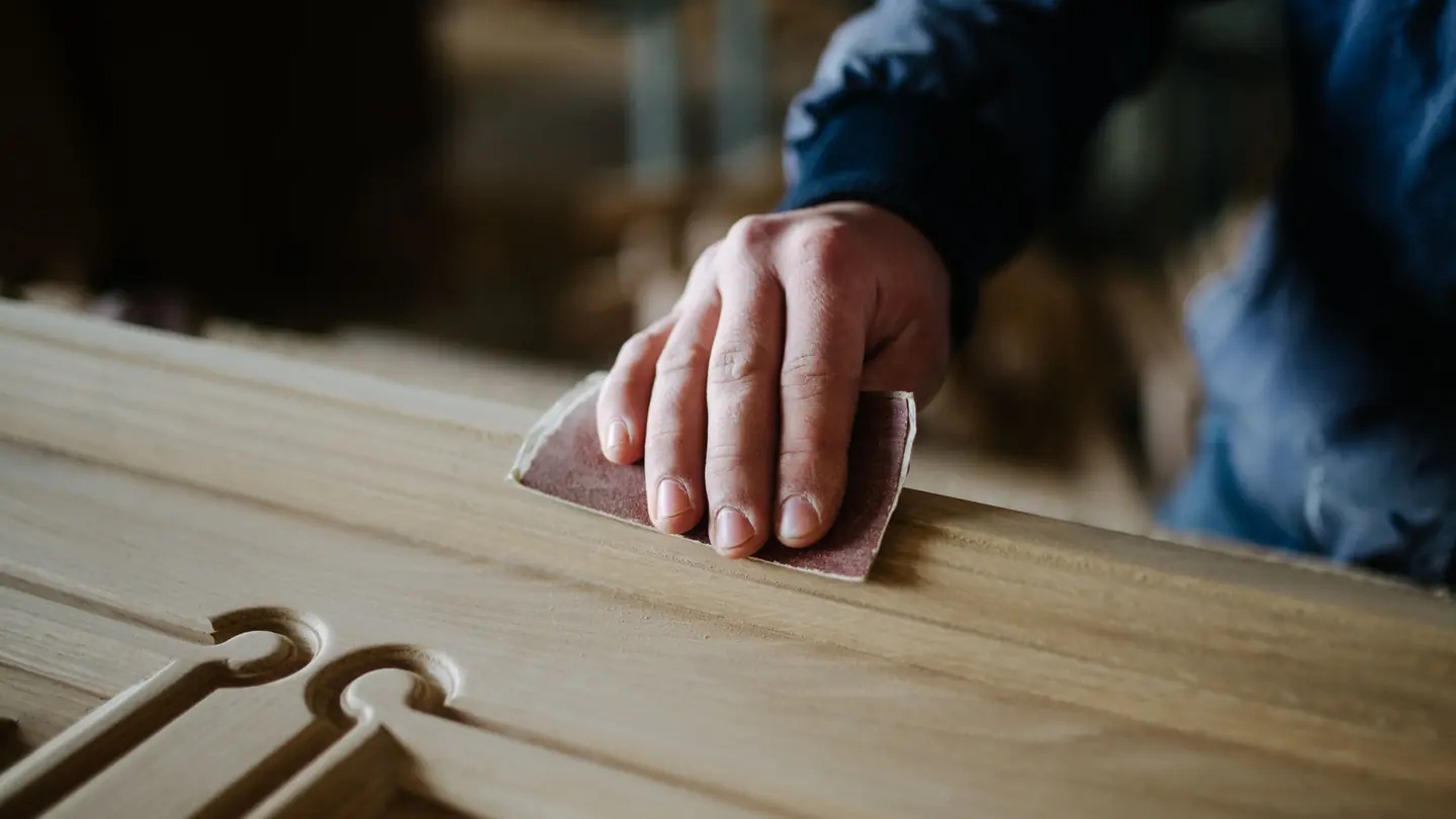 Hand eines Tischlers schleift ein helles Holzbrett in der Werkstatt