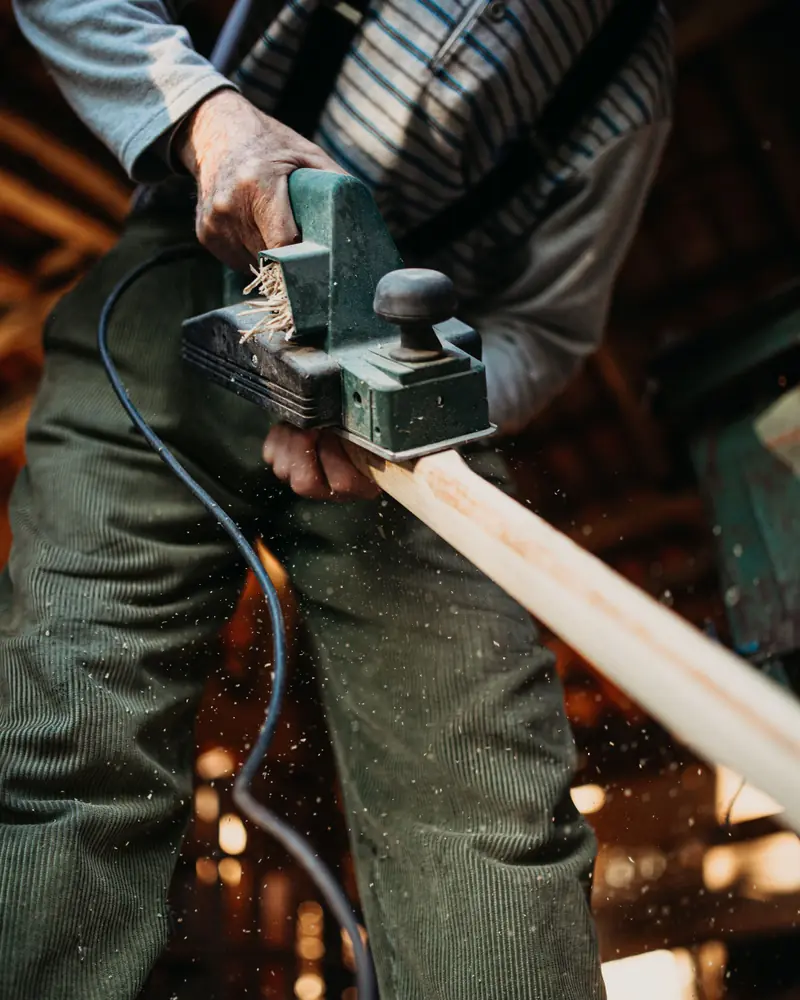 Ein Tischler führt einen Hobel über ein langes Holzbrett
