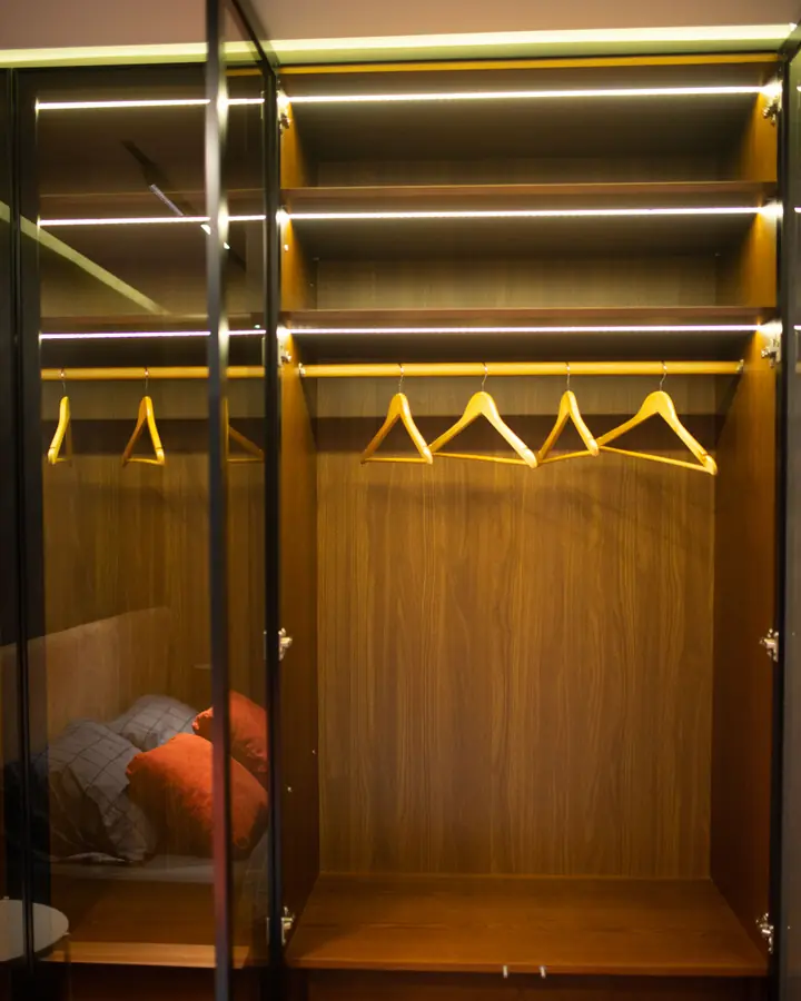 Geöffneter Einbauschrank aus Holz mit Kleiderstange und Beleuchtung