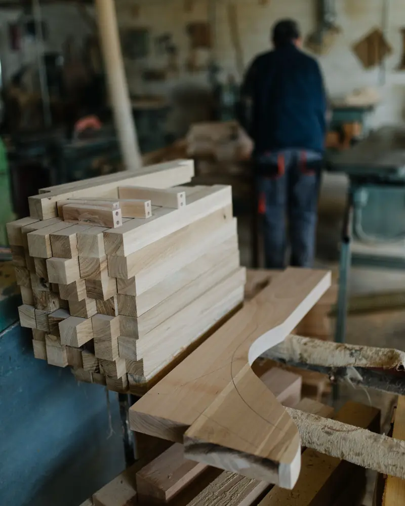 Stapel gefertigter Holzteile, im Hintergrund ein Tischler